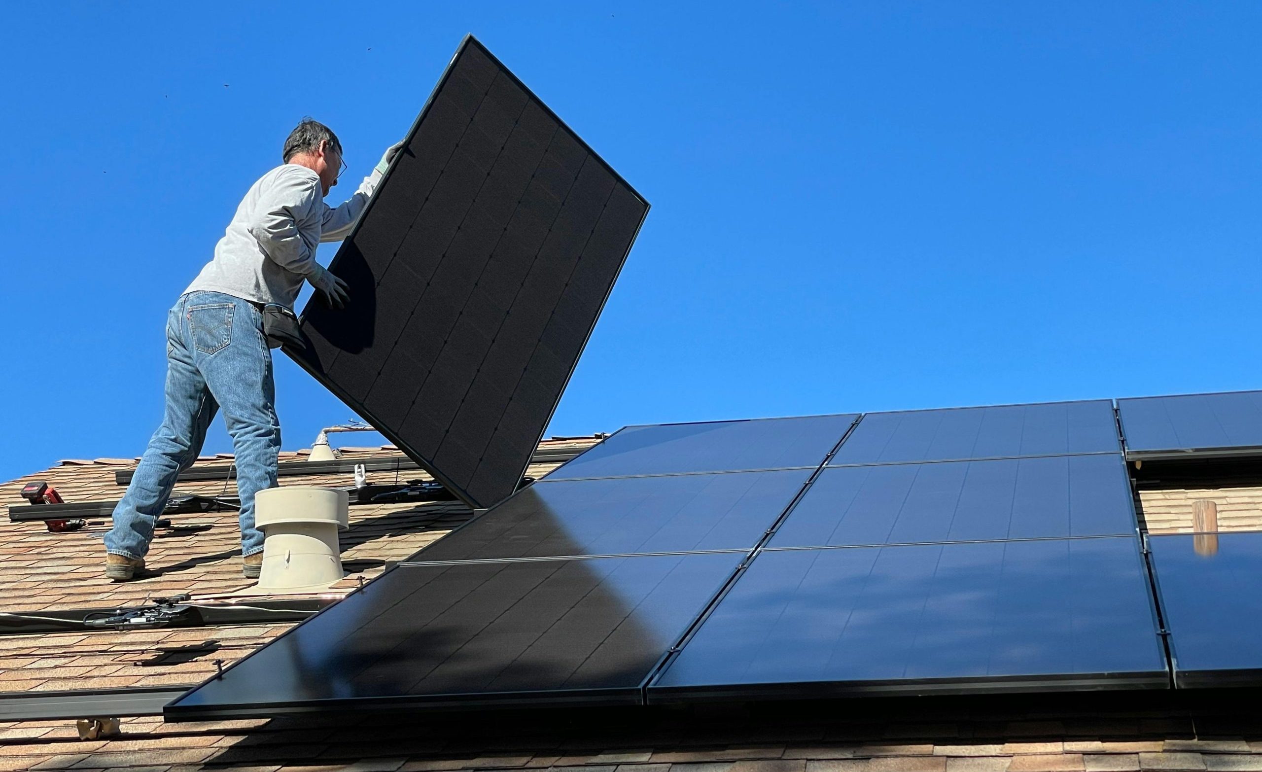 A worker installs solar panels on a sunny day, highlighting renewable energy solutions.
